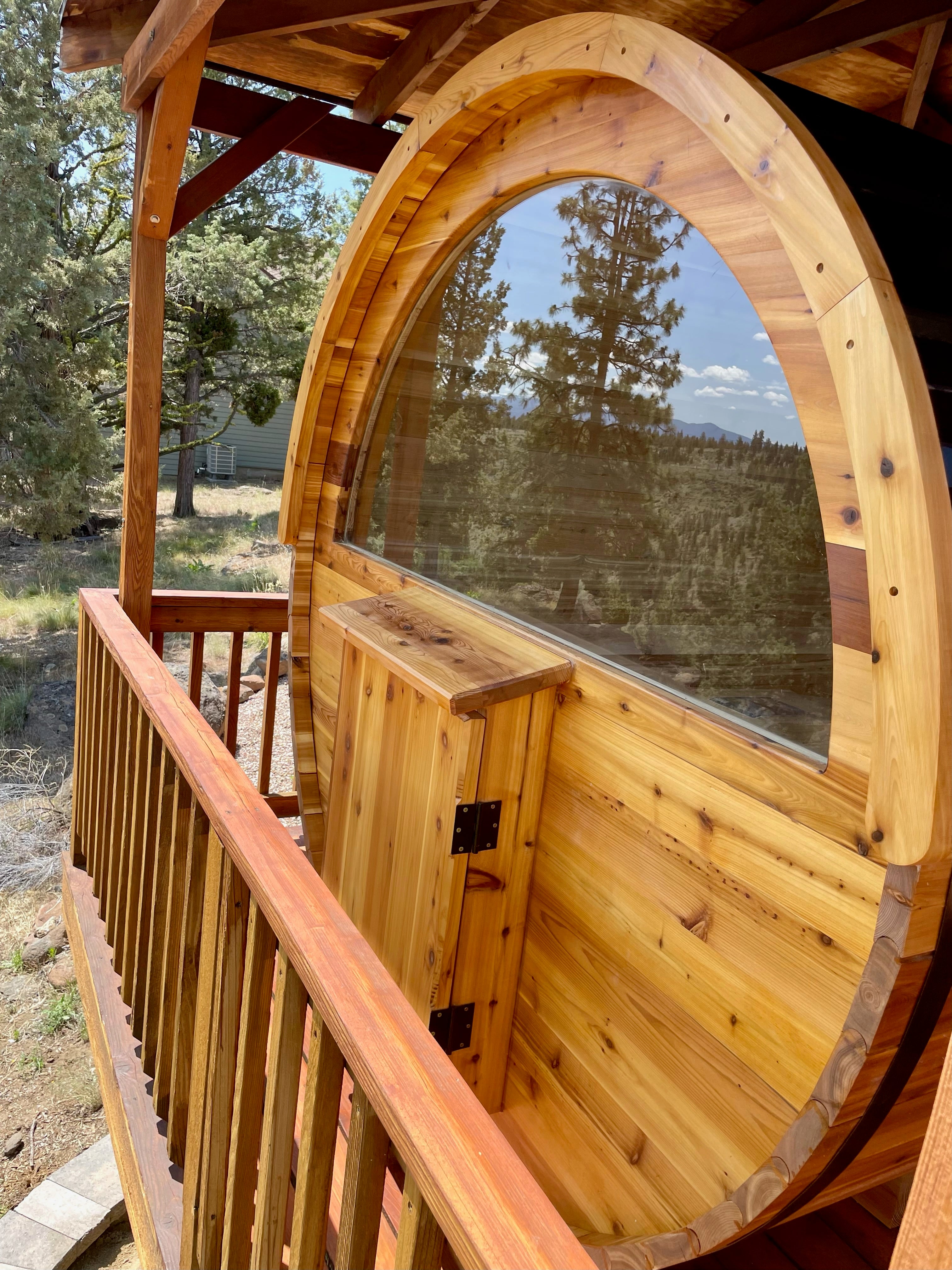 Wooden barrel sauna with an arched half window wall in a natural backyard setting