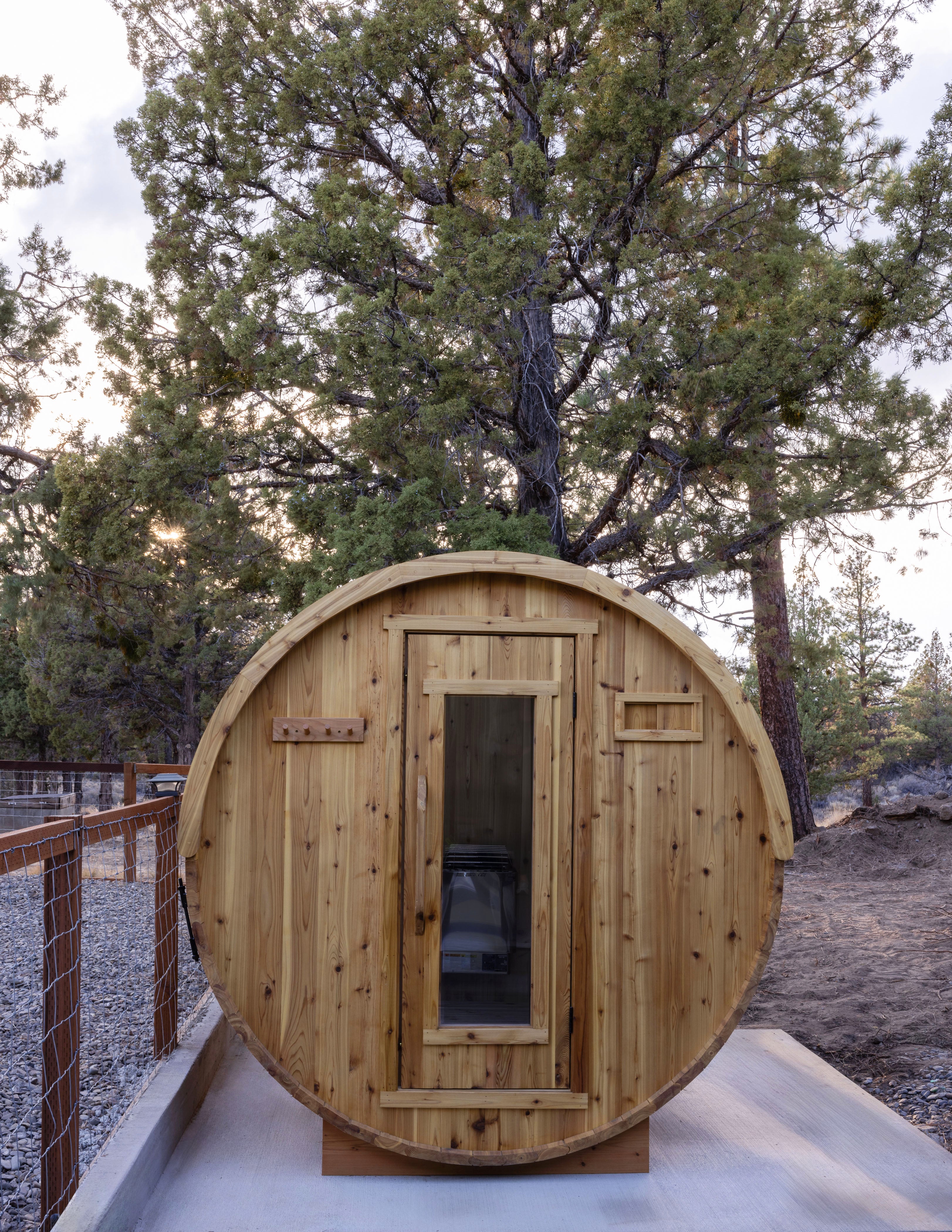 Wooden barrel-shaped structure in a natural backyard setting with trees in the background