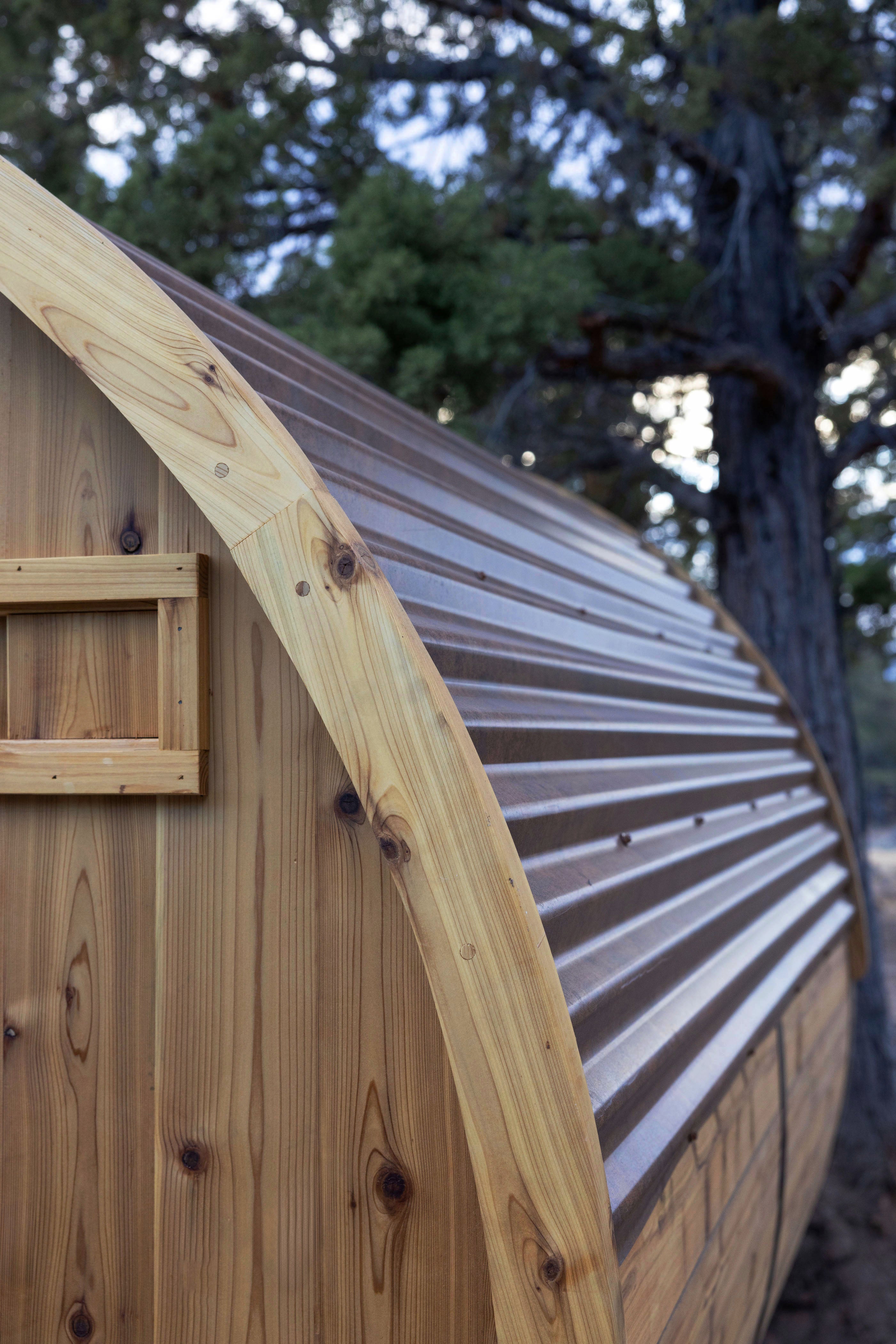Wooden barrel sauna with a metal roof in a natural setting