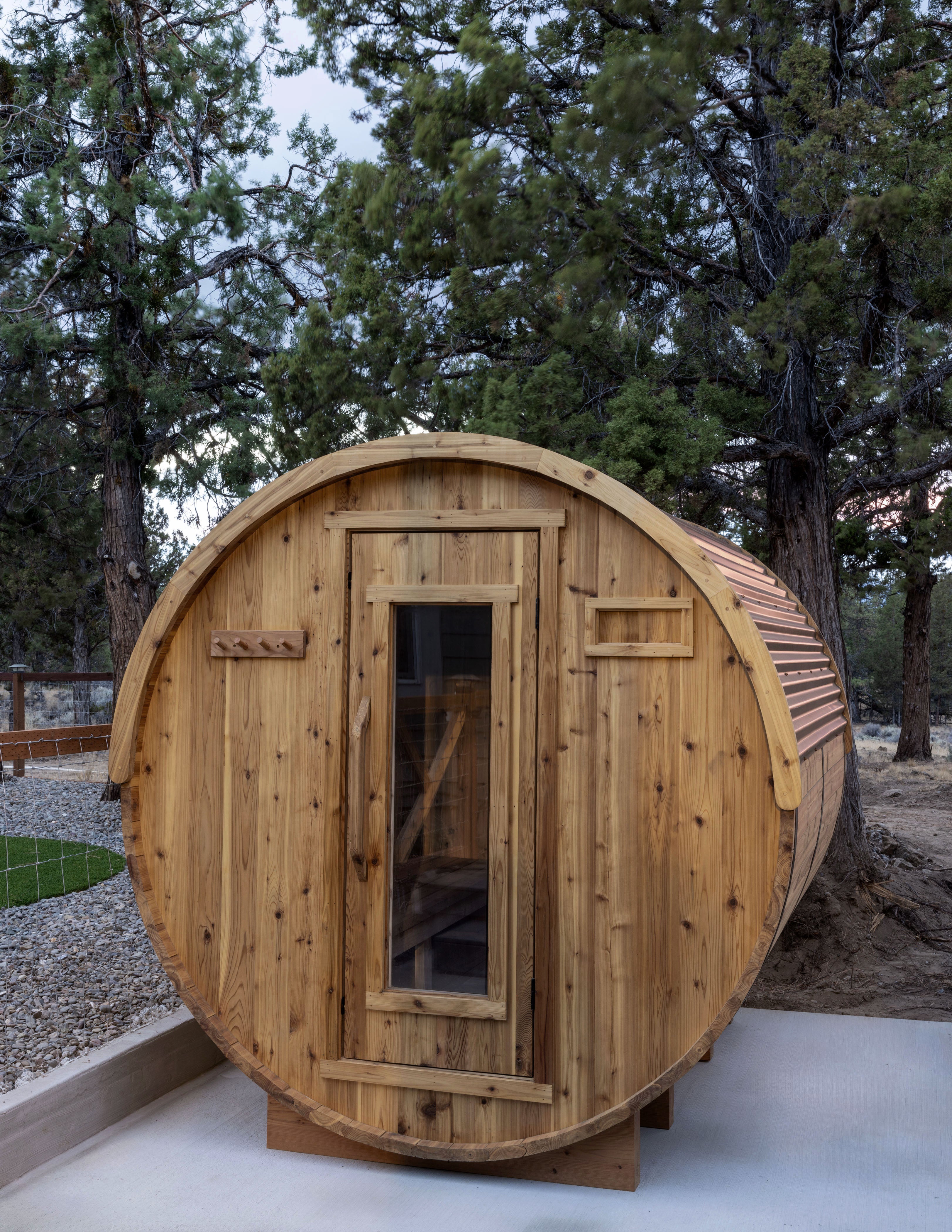 Wooden barrel-shaped sauna in a forested backyard setting